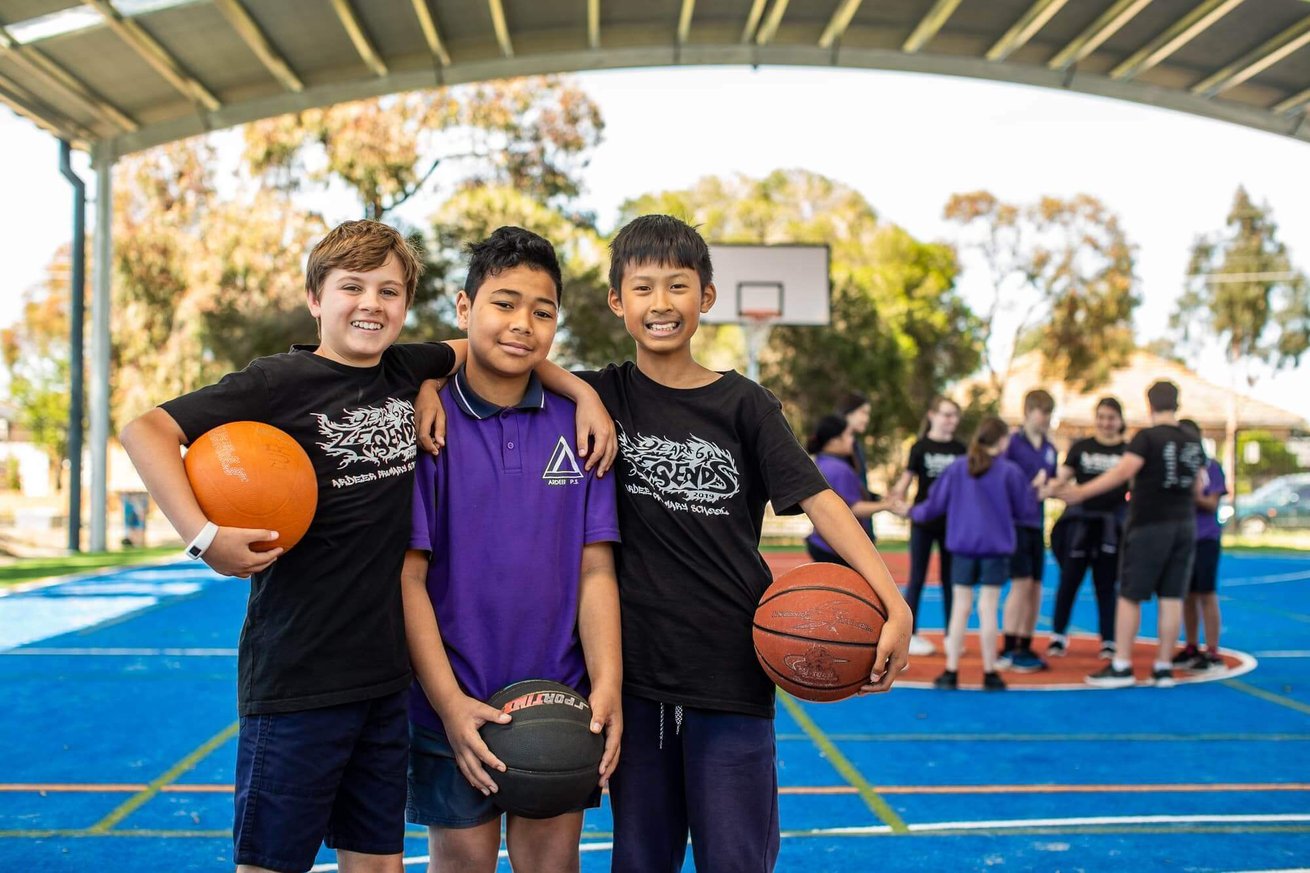 School boys with basketballs on a covered outdoor court.