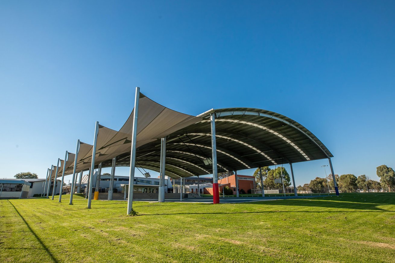 Steel-framed structure with translucent roofing in a schoolyard setting.