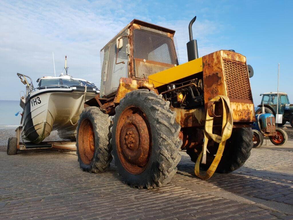 Heavily rusted tractor towing a small boat trailer parked on a concrete surface with visible wear.