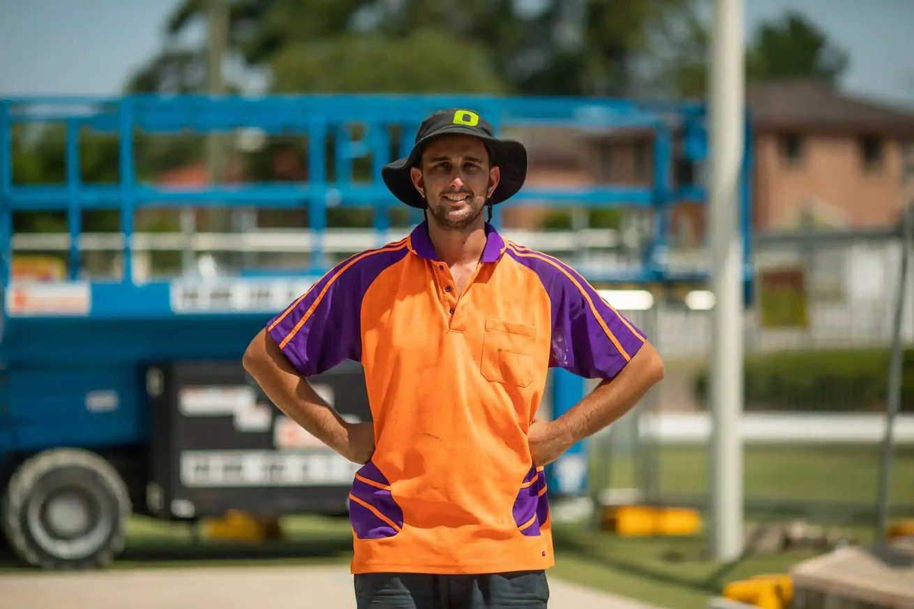 Construction worker in orange and purple uniform at outdoor job site.