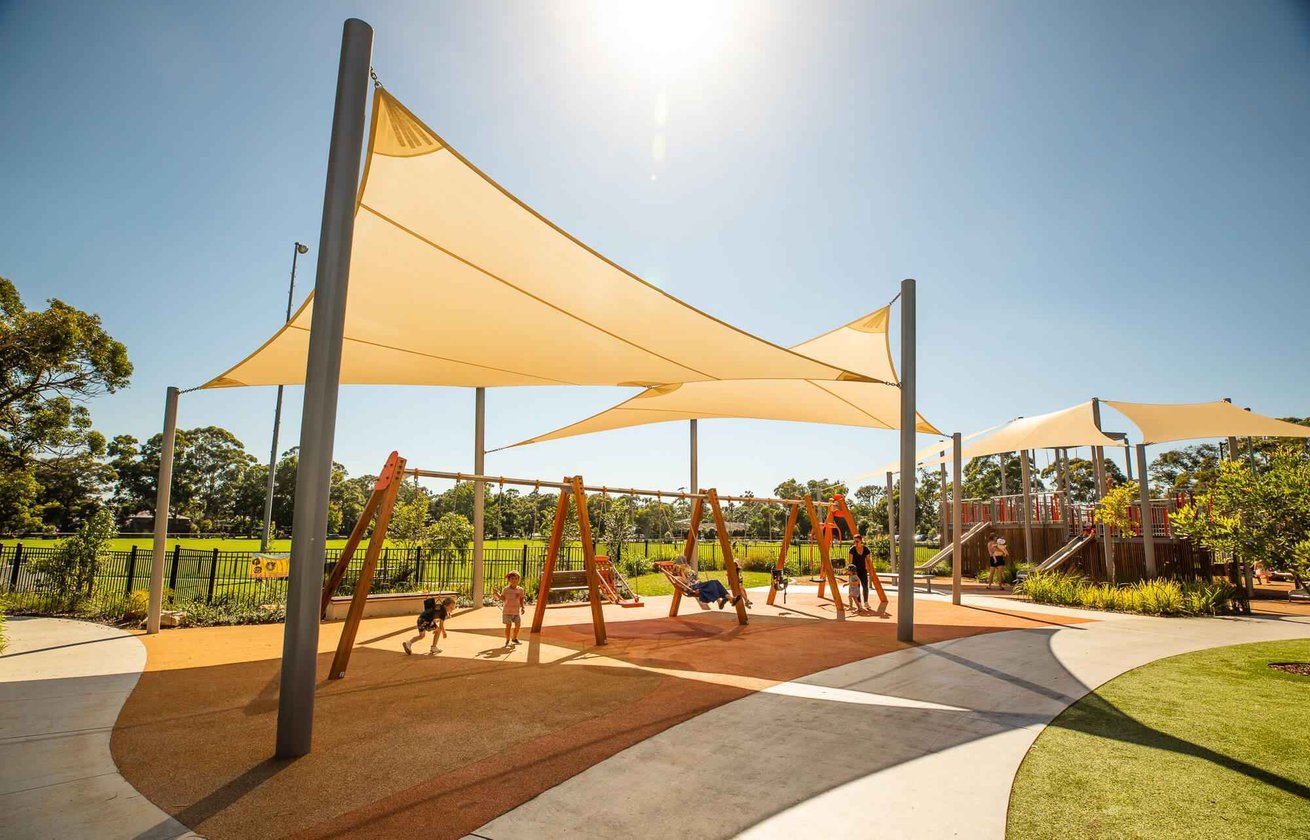 Multiple triangular shade sails in soft tones covering a paved school area, with students beneath.