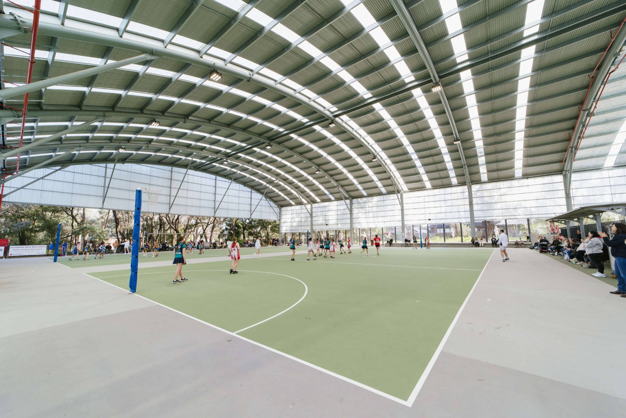 Photo of girls playing netball under the metal roof structure at Pinks Reserve Regional Netball Facility.